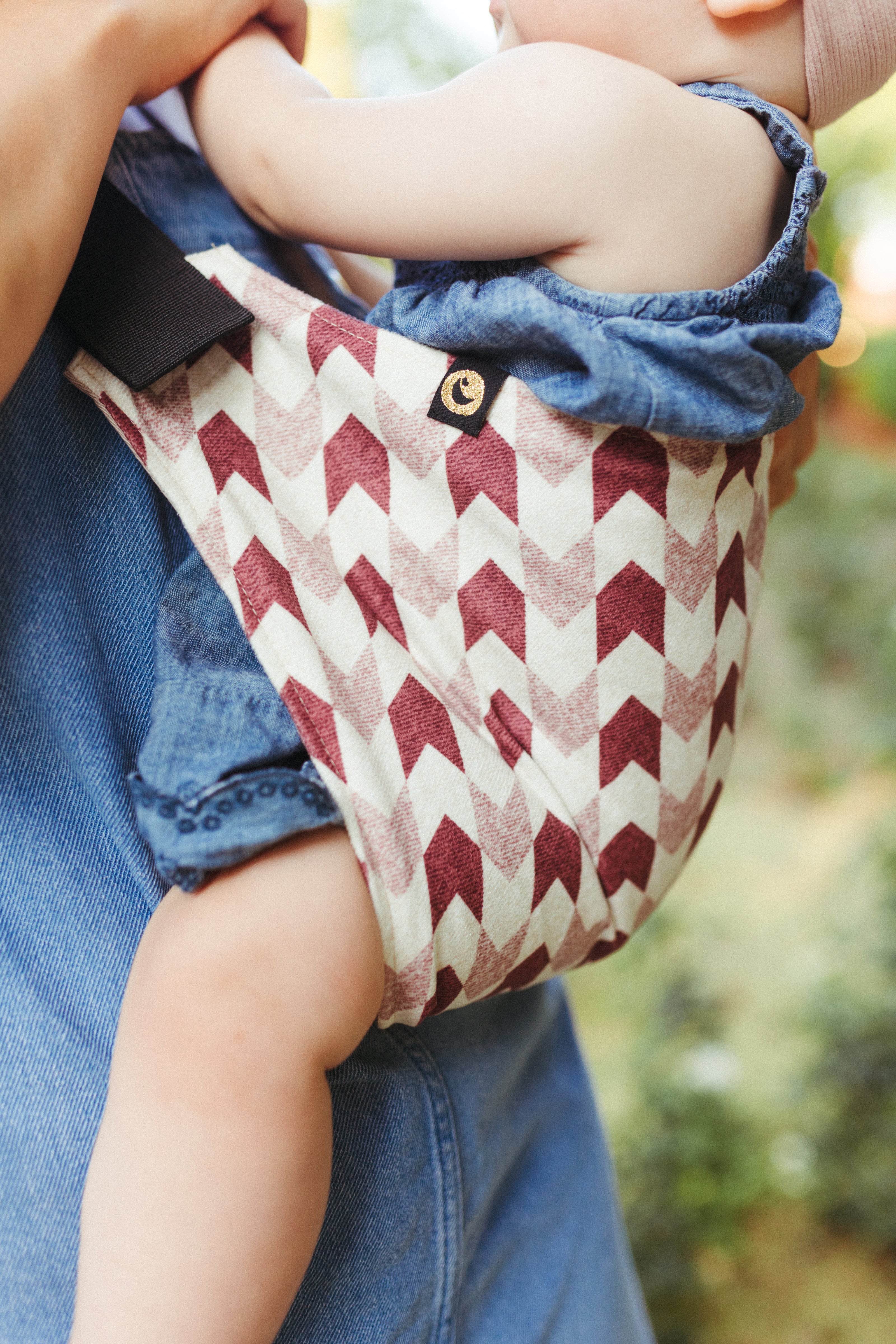 Close-up of a baby carried in the Nest for Rest Adventure Arrow toddler carrier, showcasing the carrier's durable and stylish fabric with a red and white chevron pattern.